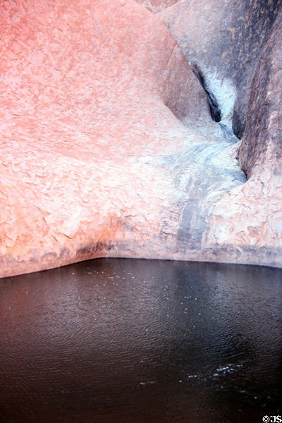 Red & blue stones of Uluru (aka Ayers Rock) meet a pool of water. Australia.
