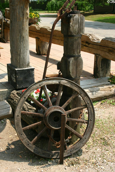 Wagon wheel leaning against antique well pump. Kleinburg, ON.