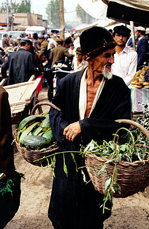 Elderly man carries baskets of vegetable waste for animal food at the Sunday market, Kashgar. China.