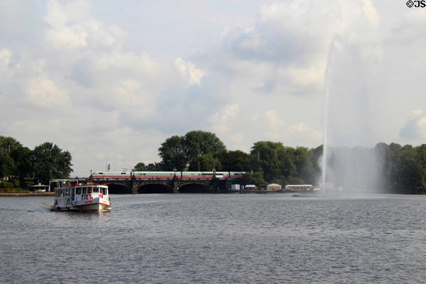 Passenger train crossing with Lake Alster fountain in foreground. Hamburg, Germany.