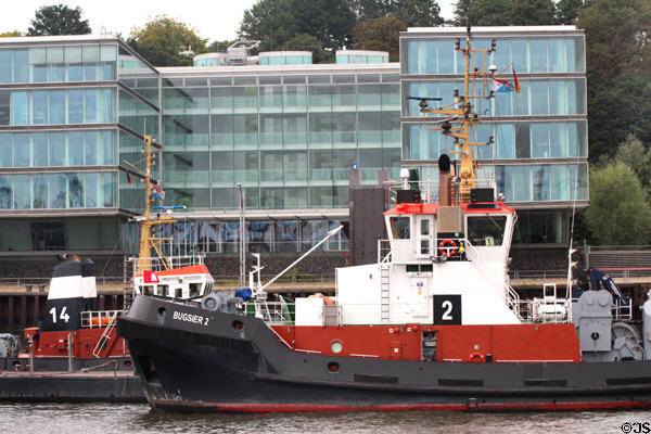 Tugboat moored on Elbe River in front of modern glass building in Altona borough. Hamburg, Germany.