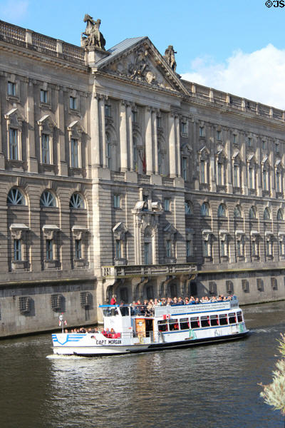 Tour boat passes palace-style facade across Spree River from Nikolaiverteil. Berlin, Germany.