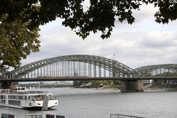 Train crossing Hohenzollern Bridge with tour boat in foreground. Köln, Germany.