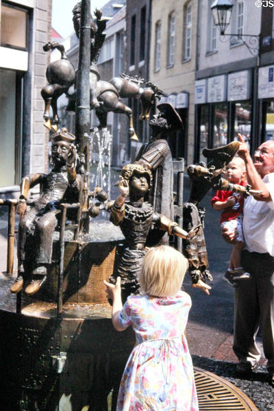 Children enjoying Puppenbrunnen, whimsical fountain featuring bronze figures of puppets with movable parts. Aachen, Germany.
