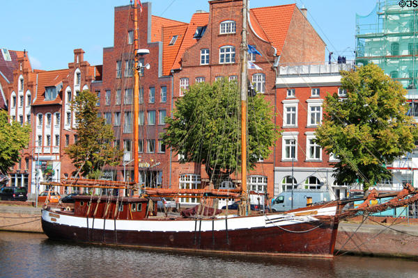 Sailing ship docked on Trave River before heritage buildings. Lübeck, Germany.