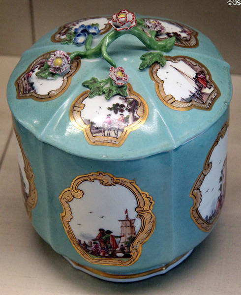 Meissen porcelain turquoise lidded vessel (c1745) with branch-shaped handle & with scenes of commercial voyages painted in white areas framed with gold at Meissen porcelain museum at Lustheim Palace. Munich, Germany.