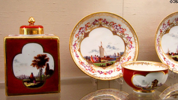 Meissen porcelain red tea service (c1740) & plate with Baroque border (c1730) with Watteau & trade travel scenes painted in white quatrefoil at Meissen porcelain museum at Lustheim Palace. Munich, Germany.