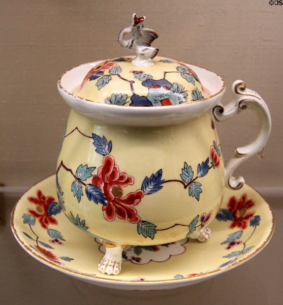Meissen porcelain yellow soup pot with knob in form of flying dragon on saucer (c1735-40) painted with red & blue Japanese-style garland at Meissen porcelain museum at Lustheim Palace. Munich, Germany.