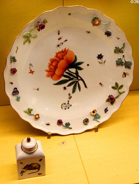 Meissen porcelain bowl (c1745) painted with peony & insects & ringed with flowers in relief beside tee box with mouse at Meissen porcelain museum at Lustheim Palace. Munich, Germany.