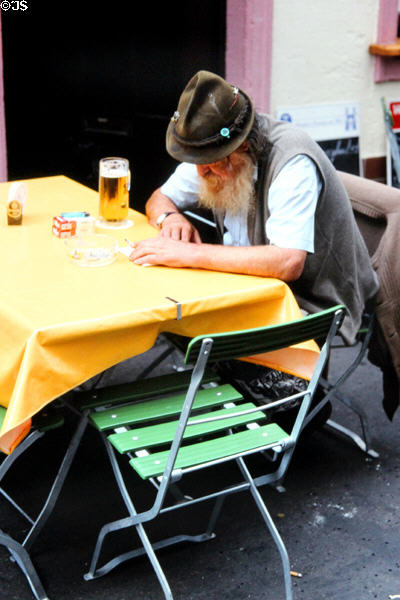 Gentleman in traditional Bavarian dress, sitting in a market square café, enjoying a beer. Würzburg, Germany.