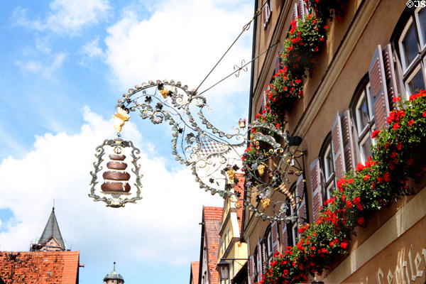 Ornate shop sign constructed with lacy metal featuring hanging basket with local pastries. Dinkelsbühl, Germany.