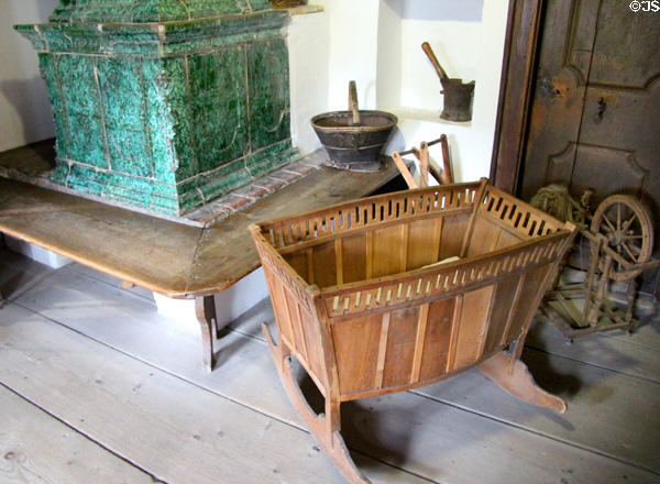 Rocking cradle & other local carvings beside tiled heating stove at Oberammergau Museum. Oberammergau, Germany.