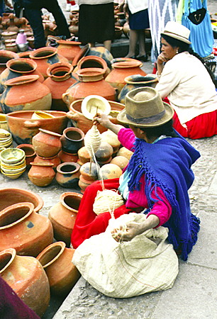 Woman spinning wool while waiting to sell pottery in the market of Cuenca. Ecuador.