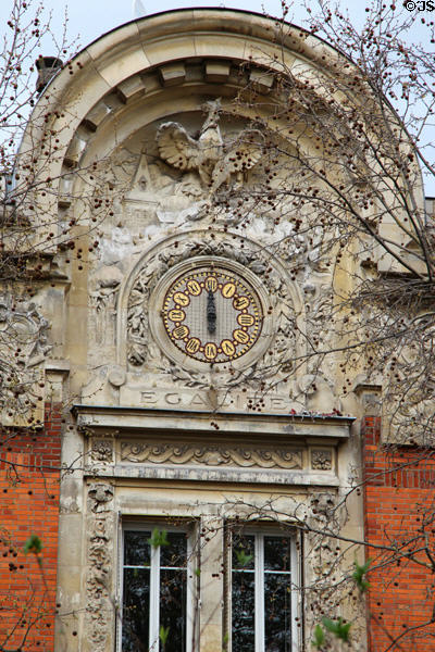 Clock on facade under carved arch in Le Marais. Paris, France.