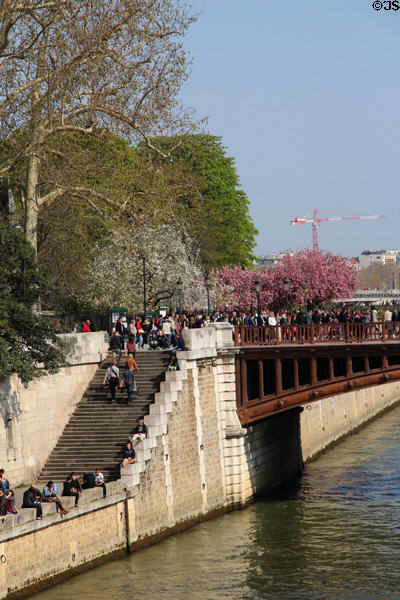 Pedestrians enjoying sunshine on quai of Seine River. Paris, France.