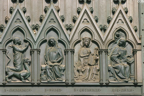 Bronze panel of central door of Cathedral showing Stes Margaret (with dragon), Agnes (with lamb), Catherine of Alexandria (with wheel of torture), Mary at the annunciation. Strasbourg, France.