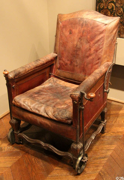 Wheelchair (c1700-10) as leather covered armchair with reclining back & crank for motion at Museum of Decorative Arts. Paris, France.