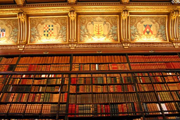 Decorative emblems bridging space between book shelves & ceiling in library at Château de Chantilly. Chantilly, France.