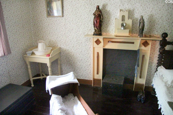 Bedroom with cradle & decorative carved fireplace surround in Mountain Farmhouse at Bunratty Castle & Folk Park. County Clare, Ireland.