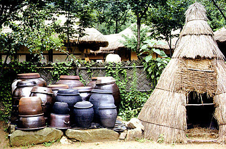 Kimch'i pots sit outside grass hut in folk village, Seoul. South Korea.