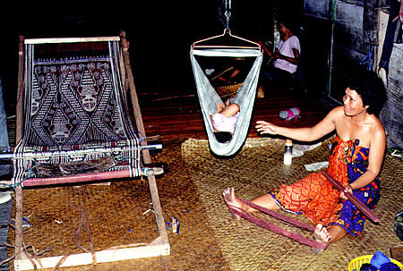 Baby swing and woman weaving in Ugat longhouse in Sarawak. Malaysia.