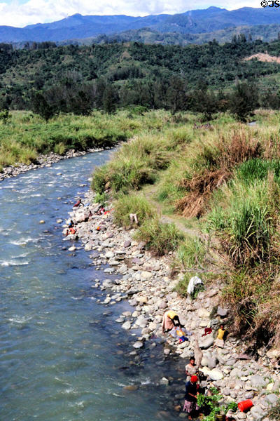 Families wash clothes by the river between Kundiawa and Minj with typical highland landscape in background. Papua New Guinea.