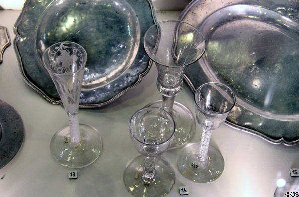 English ale glass engraved with hops leaf (c1760) & drinking glasses (18thC) with various stems in front of pewter plates at Hunterian Museum. Glasgow, Scotland.
