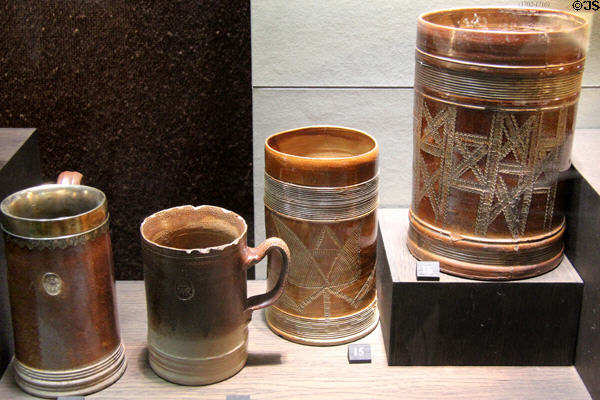 Earthenware tankards with turned decoration iron-stained brown plus additional impressed designs like royal seals (1700-10) made in North Straffordshire at Potteries Museum & Art Gallery. Hanley, Stoke-on-Trent, England.