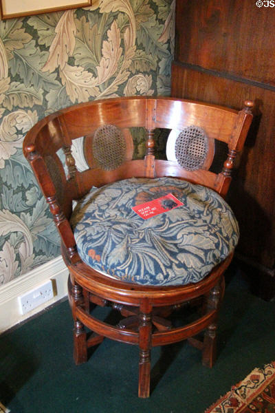 Round wooden corner chair with Morris pattern cushion against Acanthus wallpaper (1875) by William Morris at Wightwick Manor. Wolverhampton, England.