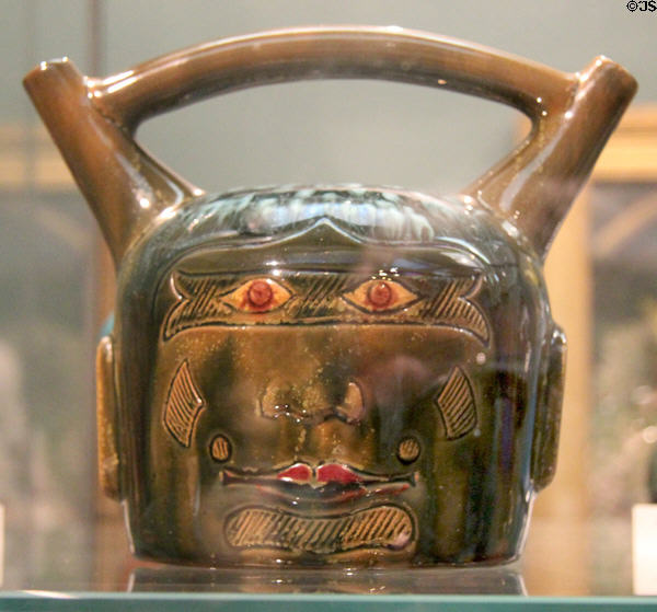 Earthenware Peruvian face bridge-spout vessel (c1880) by Christopher Dresser made by Linthorpe Art Pottery at Ashmolean Museum. Oxford, England.