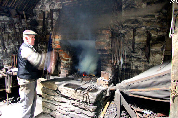 Smith working bellows at forge at Ulster American Folk Park. Omagh, Northern Ireland.