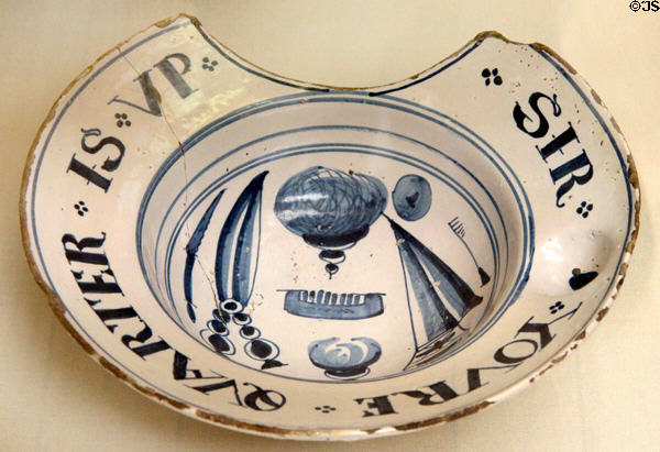 Tin-glazed earthenware shaving bowl painted with barber tools & message 'Sir youre quarter is up' since shaving bills were paid 4 times per year (c1700) from Lambeth, London at British Museum. London, United Kingdom.