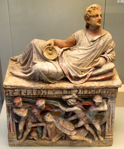 Etruscan carved terracotta cinerary urn with reclining man with libation cup on lid & battle panel on chest (150-100 BCE) from Chiusi at British Museum. London, United Kingdom.