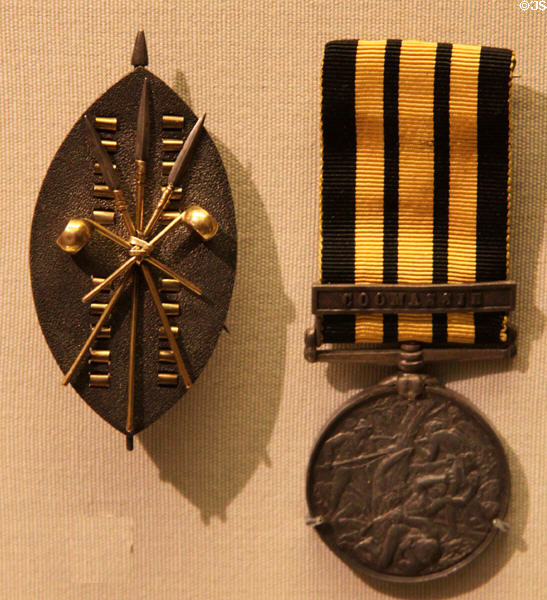 Brooch in form of Zulu shield, spears, war clubs (c1875) by John Brogden of London & medal for British troops in Assante War fought for control of Gold Coast (Ghana) (1873-4) by Edward Poynter at British Museum. London, United Kingdom.