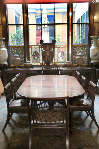 Dining table & trellis-back chairs (1821) by John Robins with sideboard with ceramics & courtyard window beyond at Sir John Soane's Museum. London, United Kingdom.