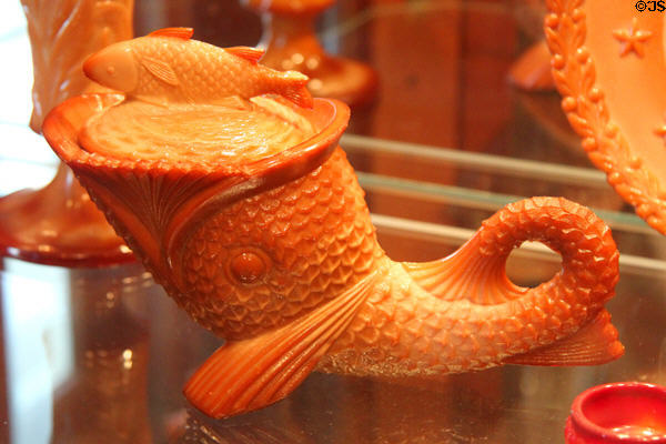 Glass dolphin with fish cover dish in orange by Greentown Glass or reproduction at Historical Glass Museum. Redlands, CA.