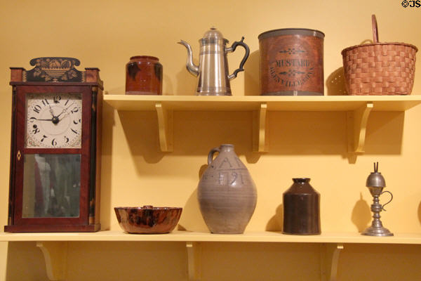 Redware jar (early 1800s), cast metal coffee pot by Hiram Yale & Co. (1824-35), mustard tin (c1858), native basket (c1840-50), shelf clock (c1809-49), redware cake mold (early 1800s), salt-glazed jug (1791) by Abraham Mead, stoneware preserve jar (late 1800s), & pewter whale oil lamp (1830-60) at Connecticut Historical Society. Hartford, CT.