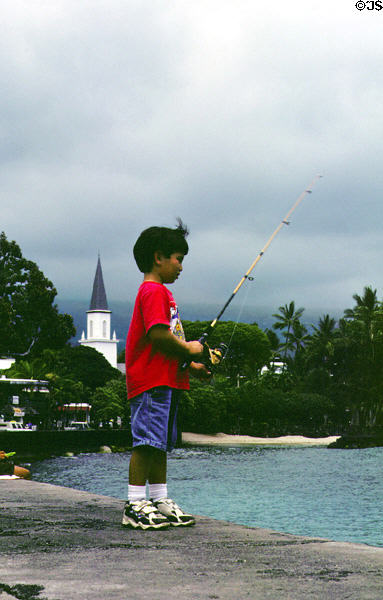 Child fishing from sea wall in Kailua-Kona. Big Island of Hawaii, HI.