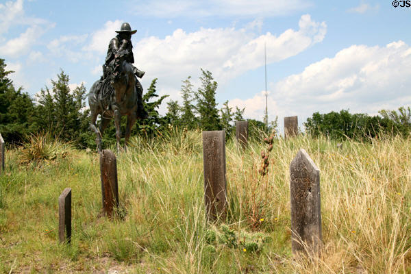 Statue of cowboy & prairie grasses surround wooden tombstones on Boot Hill Cemetery. Ogallala, NE.