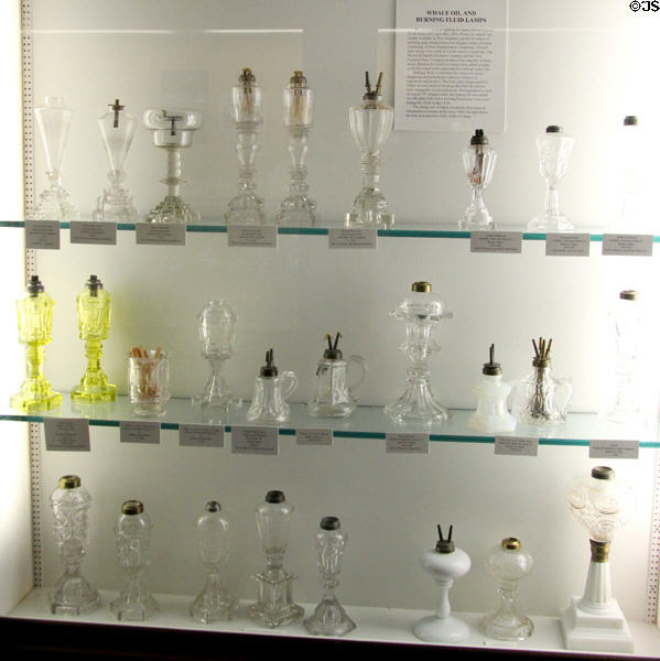 Collection of pressed glass whale oil lamps (1800s-60s) recognizable by pairs of V wicks & lack of chimney glass as found in kerosene lamps at Museum of American Glass. Milville, NJ.