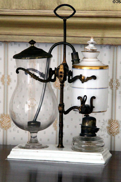 Coffeemaker on stand (mid-19thC) prob. French wherein white porcelain chambers with gold bands contains water & coffee over oil lamp heat forcing coffee through tube into glass carafe at Lindenwald. Kinderhook, NY.