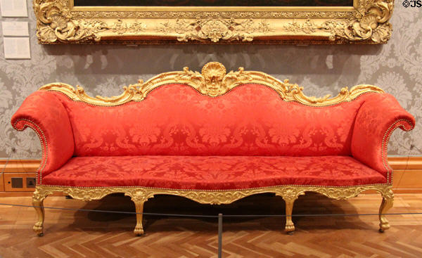 Camelback Sofa (c1767) made in London a part of 19 piece suite for Great Drawing Room at 45 Berkley Square, framed in gilt lime & beech with scarlet upholstery at National Museum of Wales. Cardiff, Wales.