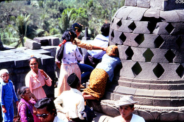 Visitors try to touch Buddha covered by stone lacework stupa at Borobudur. Indonesia.