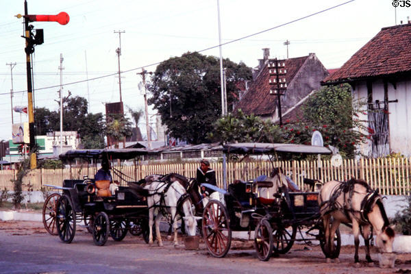 Horse-drawn carriage taxies wait outside rail station. Jogyakarta, Indonesia.