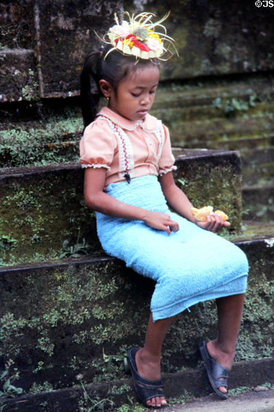 Young girl sitting at temple with offering on head. Bali, Indonesia.
