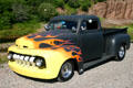 Flame-painted pickup hotrod at car rally on beach. NB.