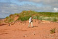 Visitor walks along red sand beach. PE.