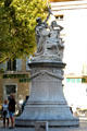 Public monument with women holding torch & mask across street from Roman Theatre. Orange, France.