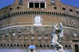 One of the Bernini angels on Sant'Angelo bridge with details of facade of Castel Sant'Angelo behind. Rome, Italy.