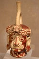 Moche ceramic stirrup-spout bottle figure of Wrinkle Face with fangs, snake ears & feline headdress from Peru at Dumbarton Oaks Museum. Washington, DC.